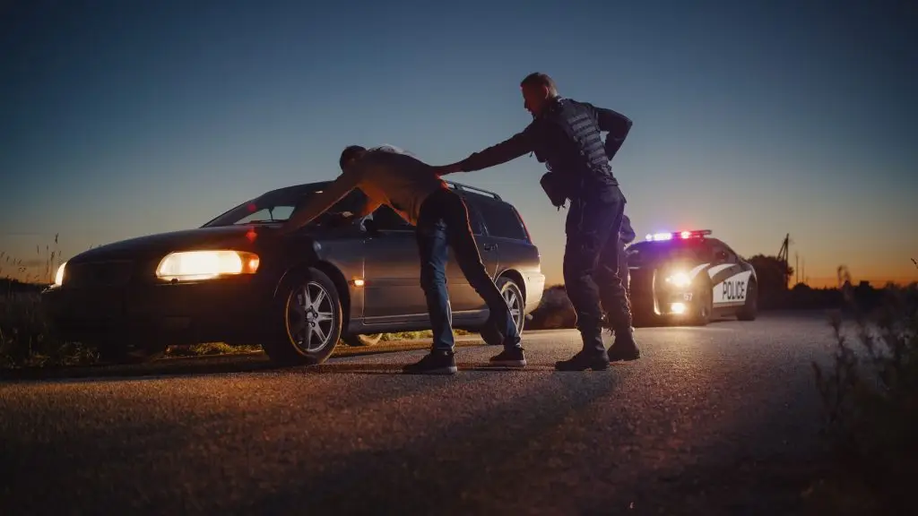 A Professional Middle Aged Policeman Performing a Pat-Down Search on a Fellon With his Hands on Car Hood. Documentary-like Shot of Procedure of Arresting Suspects.