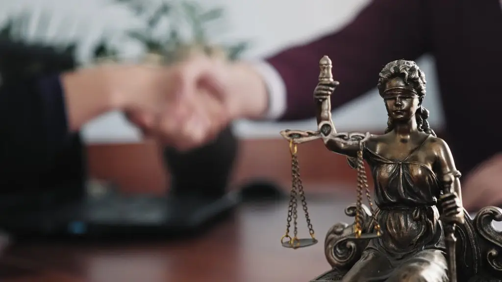 Statuette of lady justice on the table close-up against the background of the handshake of a woman and a man.