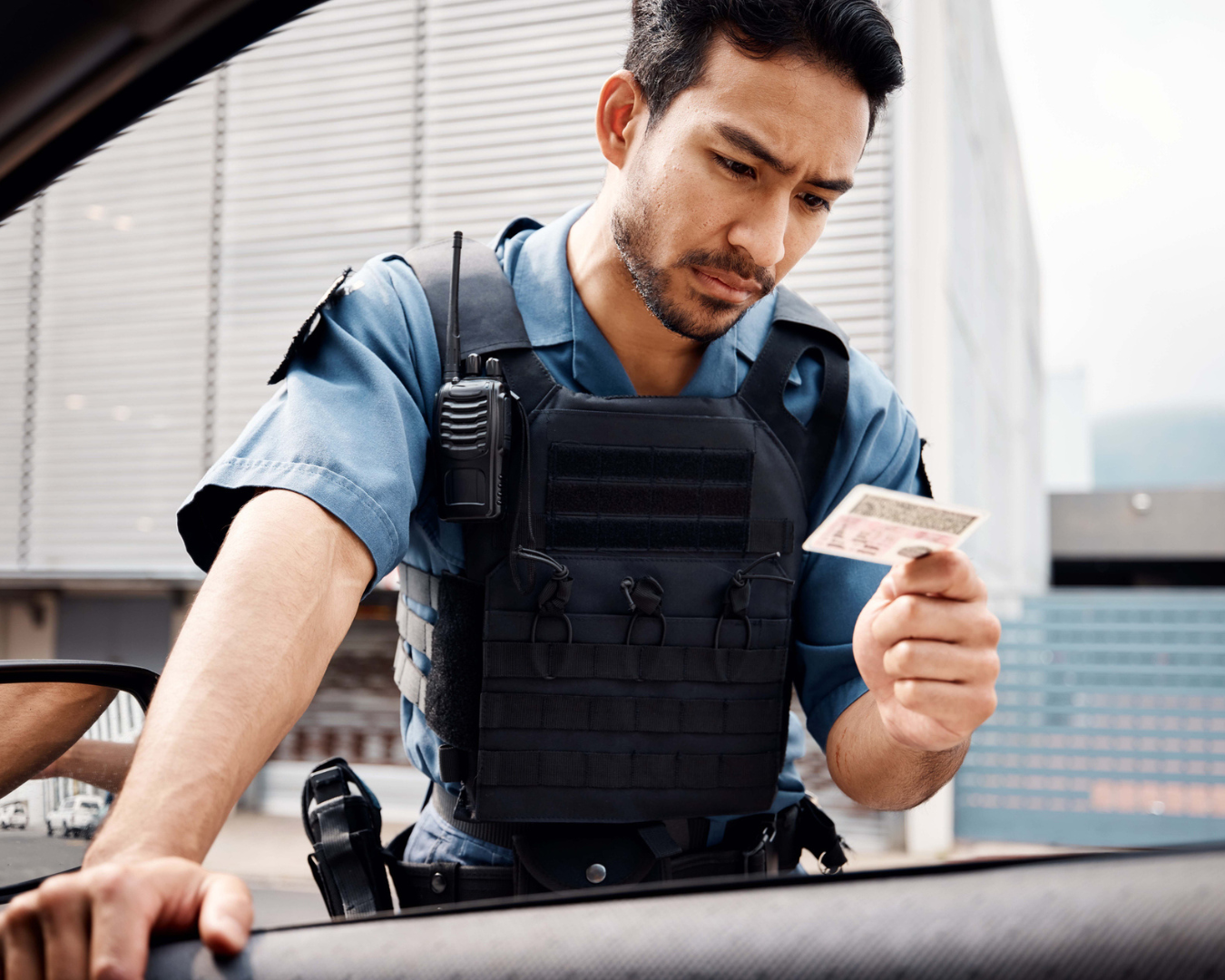 Young male police officer resting hand on car door with window rolled down, looking at license.