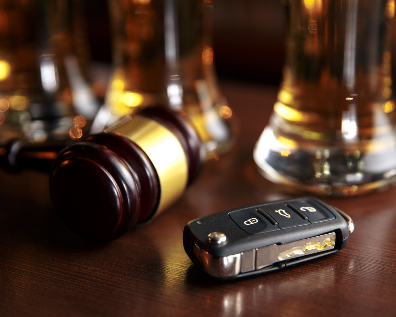 Close up of gavel resting next to keys on bar counter in front of glasses of beer.