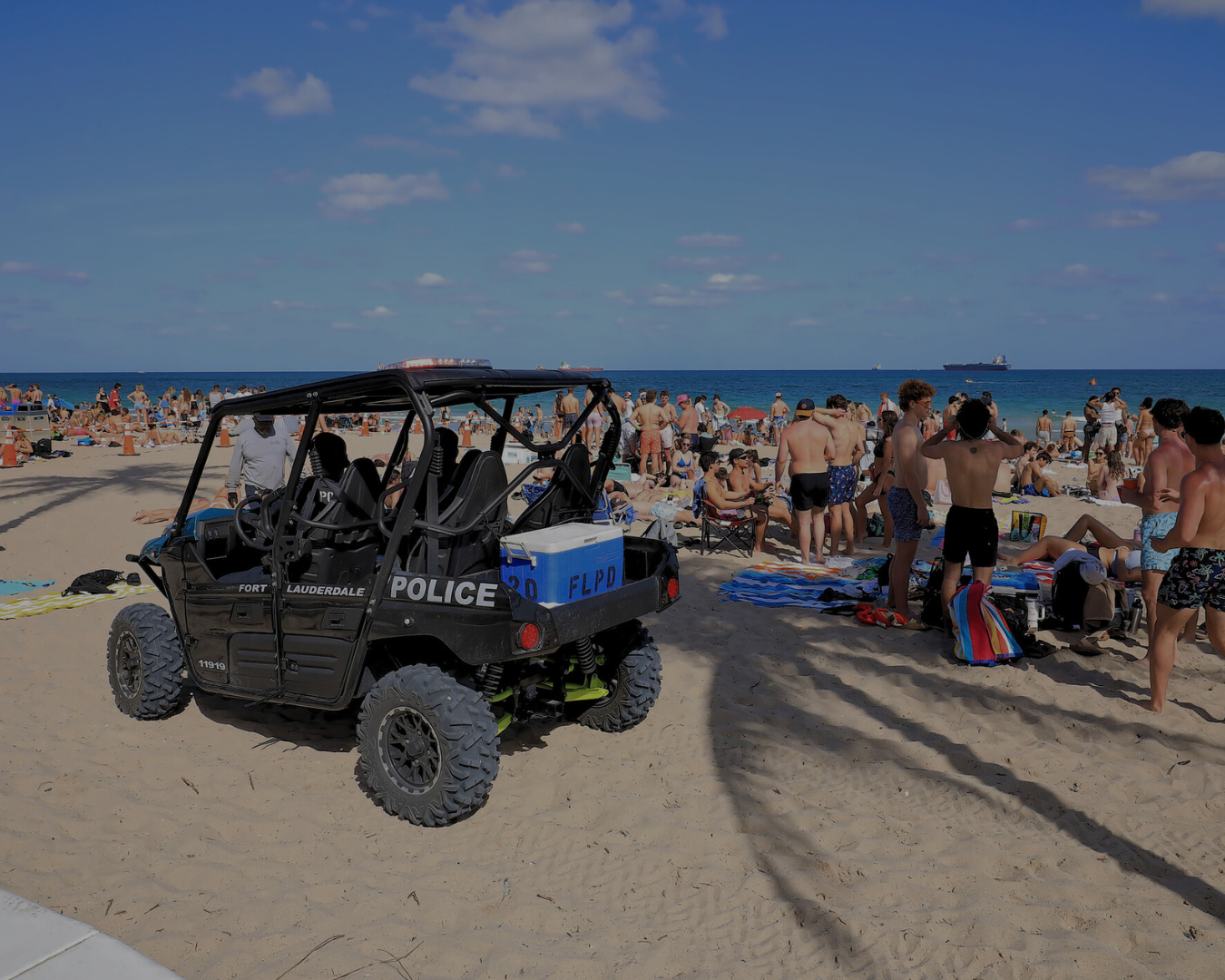Wide shot of crowded beach full of teenagers and young adults with police golf cart parked on beach.